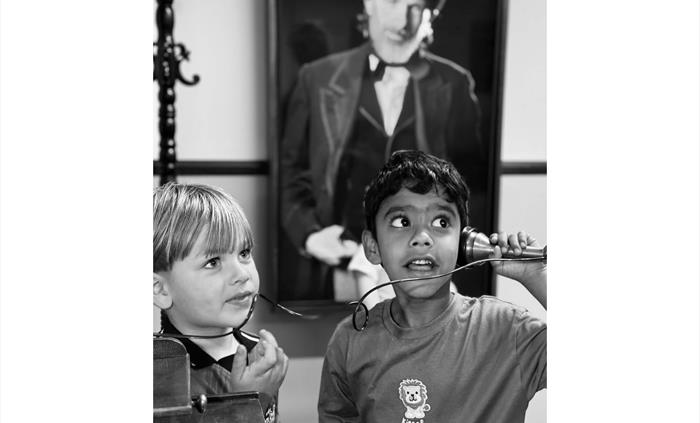 A black and white photo of two young children interacting with an old telephone from the 1800s and a picture of an industrial factory owner of the sam